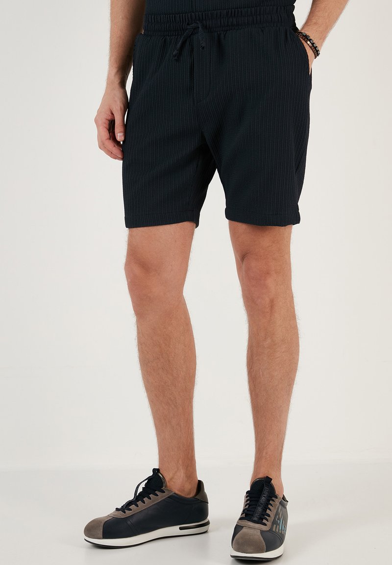 Pantaloni scurți negri cu un talie elastică și șnur, dotati cu buzunare laterale. Asortați cu adidași gri și bleumarin.