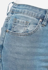Jean en denim bleu clair avec une taille mi-haute, un design à cinq poches standard, et des coutures jaunes contrastantes. Texture lisse.