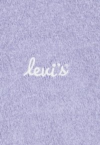 Απαλή μωβ πλεκτή ύφανση με το λευκό κεντημένο κείμενο "levi’s" σε καλλιγραφική γραμματοσειρά, με λεία υφή και ομοιόμορφες ραφές.