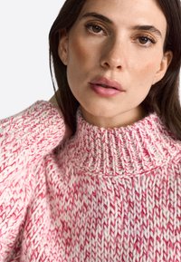 Flauschiger Strickpullover in Rosa und Weiß. Mit einem hohen Kragen und strukturiertem Muster in lockerem Schnitt. Weiches, gemütliches Material.