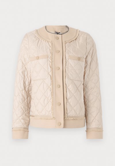Jachetă bej matlasată cu guler rotund, două buzunare frontale și închidere cu nasturi. Textură moale cu detalii de finisare contrastante.