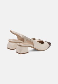 Sandalete cu toc jos, cu brâu în spate, având un corp bej și capace de vârf maro închis, curele cu cataramă pe lateral și textură de piele netedă.
