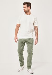 Weißes Baumwoll-T-Shirt kombiniert mit hellgrünen Cordhosen. Die Hosen haben Seitentaschen und werden mit weißen Sneakern getragen.