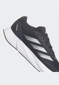 Scarpa da corsa nera con tomaia in rete, dettagli bianchi, design a tre strisce, colletto imbottito e suola spessa bianca, contrassegnata con "DURAMO" e "LIGHTMOTION."