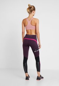 Reggiseno sportivo rosa chiaro con design a racerback, abbinato a leggings viola con accenti neri e rosa e dettagli riflettenti.