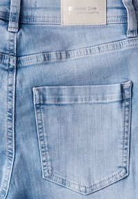 Jean en denim bleu clair avec une seule poche arrière et des détails cousus. Le tissu est doux et légèrement fané pour un aspect usé.