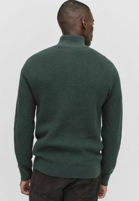 Ciemnozielony sweter z prążkowanej tkaniny, z wysokim kołnierzem i długimi rękawami, z dopasowaną talią i teksturowanym wzorem dzianiny.
