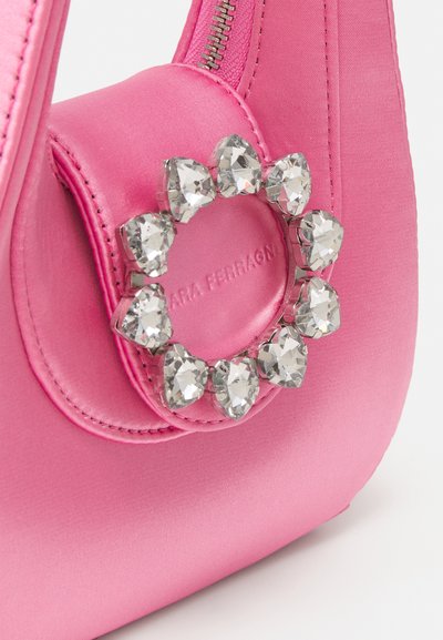 Sac à main en satin rose avec une forme arrondie et un accent de bague en cristal décoratif sur le devant. Texture lisse avec des détails cousus.