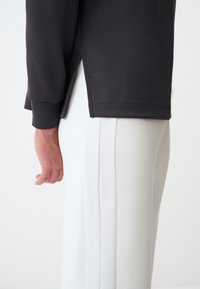 Maglietta nera a maniche lunghe con dettaglio di fessura laterale, abbinata a pantaloni grigi chiari con righe texturizzate lungo i lati.