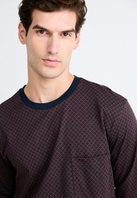 T-shirt à manches longues à col rond bleu marine avec un motif en losanges, présentant une poche poitrine et une texture de tissu douce.
