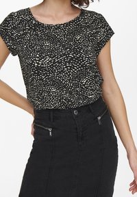 Haut noir avec motif abstrait blanc, col rond et manches courtes, associé à une jupe en denim noire taille haute avec des fermetures éclair.