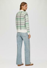 Strickpullover mit hellem Grundton, der grüne und schwarze horizontale Streifen aufweist. Kombiniert mit hoch taillierten, hellblauen weit geschnittenen Jeans.