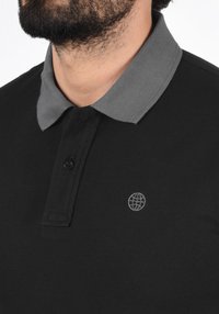 Čierne polo tričko so sivým golierom, ktoré má dvojité zapínanie na gombíky a malé vyšívané logo globusu v sivej farbe na hrudi.