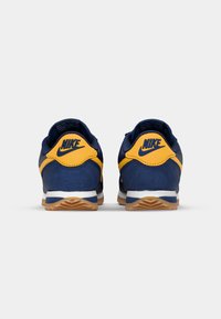 Plave i žute Nike tenisice s gornjim dijelom od antilopa i sintetičkih materijala, bijelom srednjom podrškom za jastučenje i đonom od gume. Stražnja strana prikazuje logo.