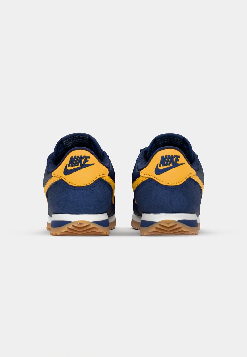 Baskets Nike bleu et jaune avec une tige en daim et synthétique, une semelle intermédiaire blanche et une semelle extérieure en caoutchouc gomme. La vue de dos met en avant le logo.