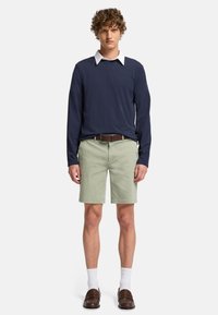Marine langærmet skjorte med hvid krave, parret med lysegrønne shorts. Brun bælte, hvide strømper og brune slip-on sko fuldender outfittet.