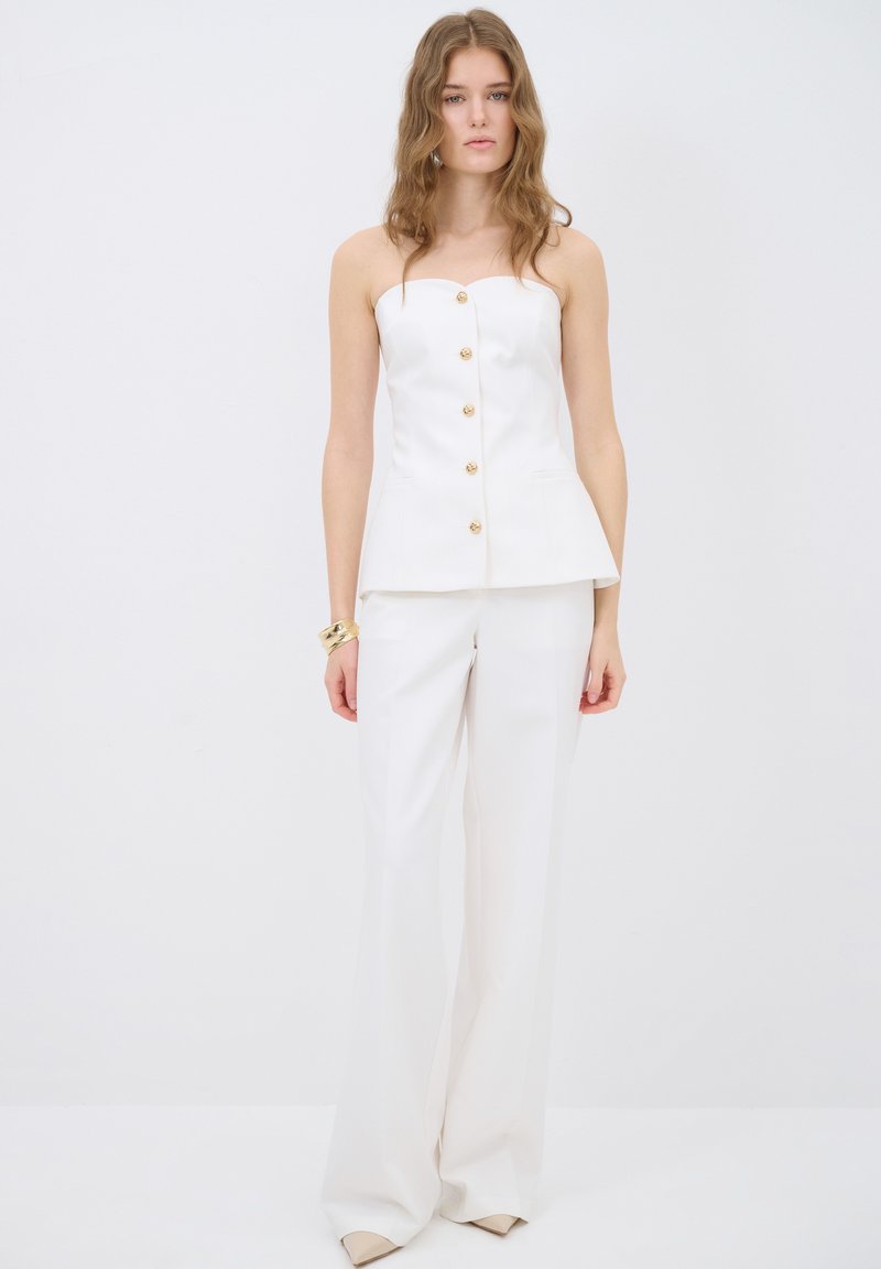 Witte peplumtop met gouden knopen, gecombineerd met witte wijde broek. Gladde stof, strapless ontwerp en minimalistische accenten.