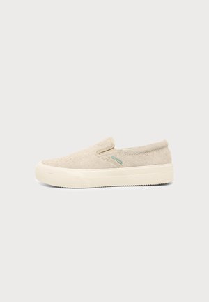 Baskets beige clair à enfiler avec tige en tissu texturé et semelle épaisse en caoutchouc blanc cassé sur fond uni.