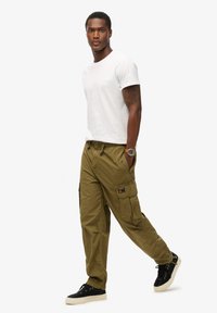 Olijfgroene cargobroeken met zijzakken, gecombineerd met een wit T-shirt met ronde hals. Zwarte sneakers met een crème-zool. Casual outfit, eenvoudig ontwerp.