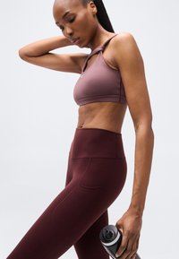 Completo sportivo composto da un reggiseno sportivo color malva chiaro con design a spalline intrecciate e leggings bordeaux a vita alta con tasche laterali.