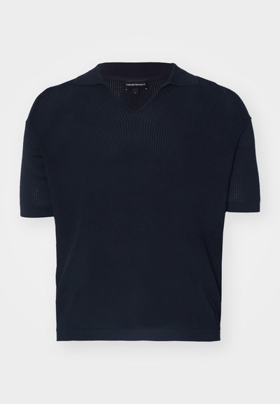 Tamsiai mėlynas megztas polo marškinėliai su V formos iškirpte, trumpomis rankovėmis ir banguota tekstūra. Yra klasikinis apykaklė ir laisvas siluetas.