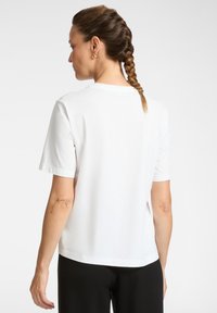 Witte katoenen T-shirt met korte mouwen, ronde halslijn en een rechte snit. Heeft zijsplitten aan de hoek voor extra bewegingsvrijheid.