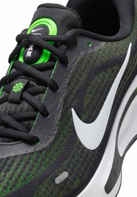 Sort og grøn atletisk sko med tekstureret stof, hvid swoosh, grønne detaljer og snørebåndsdesign. Har en polstret sål og forstærkede øjer.