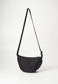 Bolso de hombro negro de tela con forma curva, correa ajustable y cierre con cremallera, que presenta una superficie texturizada y un diseño suave.