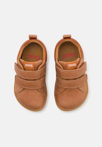 Braune Lederschuhe mit Klettverschluss, abgerundetem Zehenbereich und Gummisohle. Das Innere verfügt über gepolsterte Einlagen und pinkes "CAMPER"-Branding.