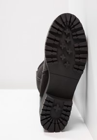 Suola di stivale nera con un motivo di battistrada robusto, caratterizzata da scanalature e sezioni rialzate per una migliore aderenza, realizzata in un materiale gommoso resistente.
