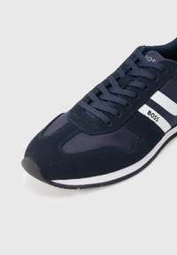 Baskets bleu marine en daim et mesh, avec des lacets assortis et des accents rayés blancs sur les côtés. Semelle en caoutchouc légère.