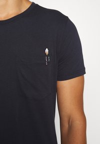 Tmavě modré bavlněné tričko s kulatým výstřihem a krátkými rukávy. Uprostřed má náprsní kapsu s malou, barevnou vyš�ívanou zmrzlinou.