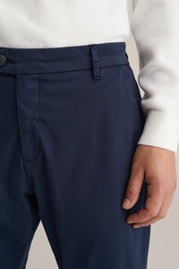 Marineblaue Hose aus strukturiertem Stoff mit tailliertem Schnitt. Verfügt über eine Vorderseite-Tasche, einen Knopfverschluss und ein scharf geschnittenes Taillenbanddetail.