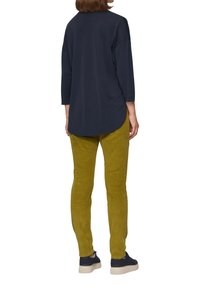 Marineblaue, locker sitzende Bluse mit 3/4-Ärmeln, kombiniert mit olivgrünen, schmal geschnittenen Hosen und marineblauen Sneakers mit strukturierten Sohlen.