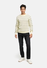 Lys gulstribet sweater med rund hals, parret med mørke jeans og hvide sneakers. Har ribbede manchetter og kant.