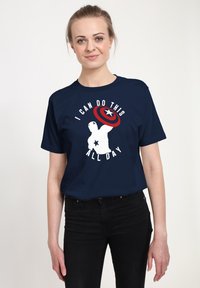 Námořnická modrá trička s krátkým rukávem, na kterém je bíly text "TOHOTO MŮŽU DĚLAT CELOU DOBU" a grafika štítu kapitána Ameriky a jeho siluety.