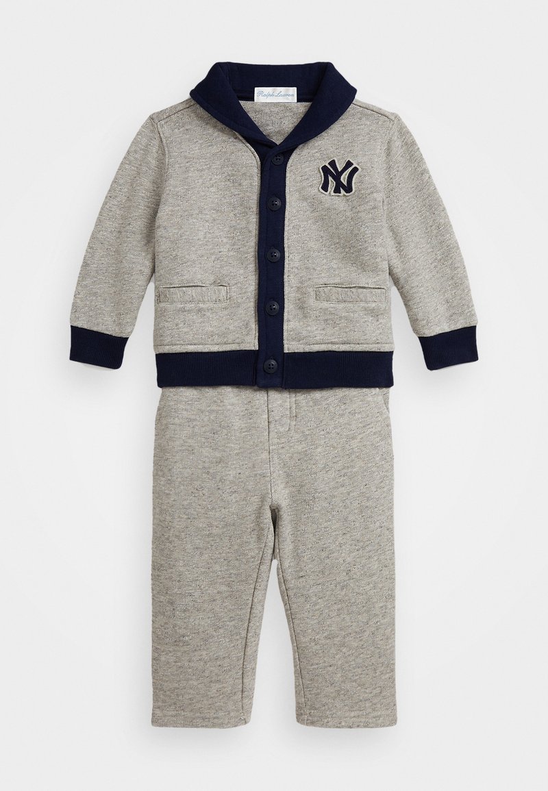 Γκρι πλεκτή δύο κομματιών εμφάνιση που περιλαμβάνει ένα πουλόβερ με κουμπιά και ναυτική γιακά, συνδυασμένο με αντίστοιχο παντελόνι. Μάινδαμα μαλακή υφή σε όλη την επιφάνεια.