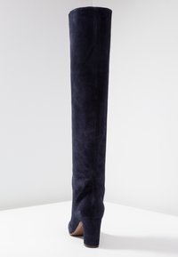 Stivale in suede blu navy al ginocchio con tacco alto. Design elegante con una texture liscia e un dettaglio di cucitura sottile lungo la parte posteriore.