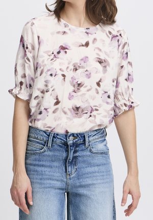 Blusa con motivo floreale in tessuto leggero con sfumature di rosa e viola, scollatura rotonda e maniche corte leggermente arricciate, abbinata a jeans in denim blu.