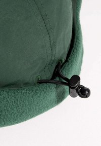 Vihreä fleecevuorattu hattu, jossa on teksturoitu ulkopinta. Varustettu mustalla säädettävällä nauhalla, jossa on kiristin alaosassa mukautettavuutta varten.