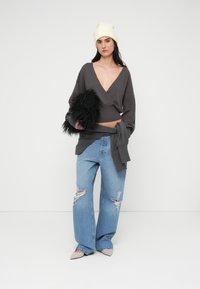 Γκρι κοντό πουλόβερ με λαιμόκοψη σε σχήμα V, σε συνδυασμό με σκισμένα ανοιχτόχρωμα τζιν. Το μοντέλο κρατάει αξεσουάρ μαύρης τεχνητής γούνας και φοράει εκρού σκουφάκι.