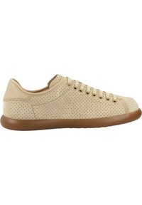 Sneaker in pelle beige perforata con punta arrotondata, suola piatta in gomma marrone e lacci frontali. Presenta un design minimalista e una texture liscia.