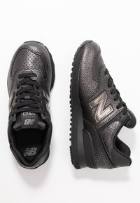 Schwarze Sportschuhe mit strukturiertem Synthetik-Obermaterial, ausgestattet mit einem silbernen "N"-Logo, Schnürsenkeln und einer Gummisohle mit robustem Profil.