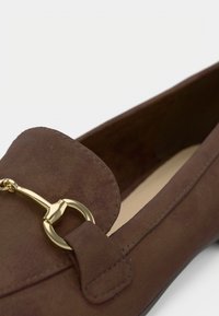 Rjavi semiš čevlji z okroglo konico in zlatim kovinskim dodatkom. Čevlji imajo ravno podplat in všite poudarke ob robovih.