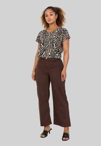 Black and tan zebra-print short-sleeve top paired with high-waisted brown wide-leg pants and black heeled mules on a gray background.
