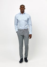 Lichtblauw overhemd met lange mouwen, grijze joggingsbroek met trekkoord en marineblauwe sneakers. Gladde stof en een getailleerde pasvorm.