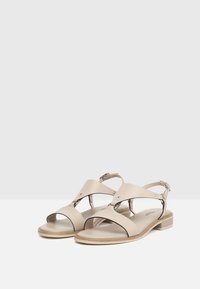 Sandales en cuir beige avec un design à lanières croisées, bout ouvert et un petit talon en bois. Comprend une boucle réglable et un discret détail de perforation.