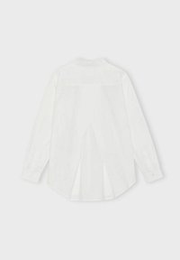 Camicia bianca a maniche lunghe con yoke posteriore alto, dettaglio della piega sul retro, polsini con bottoni e orlo curvo. Tessuto di texture liscia.