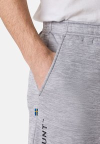 Harmaat urheilu joggerit, joissa on teksturoitu kuvio, sivutasku ja pieni Ruotsin lipun yksityiskohta helmassa sekä logo painettuna sivulle.
