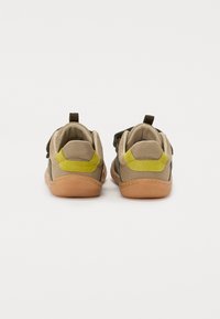 Zapatos de malla marrones y verdes con suela de goma, que presentan un acento amarillo en el talón y una correa para un ajuste seguro.